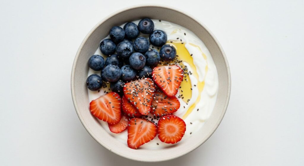 A top-down view of a breakfast bowl with Greek yogurt, blueberries, strawberries, chia seeds, and a honey drizzle that are a good option for Anti-Inflammatory Foods.